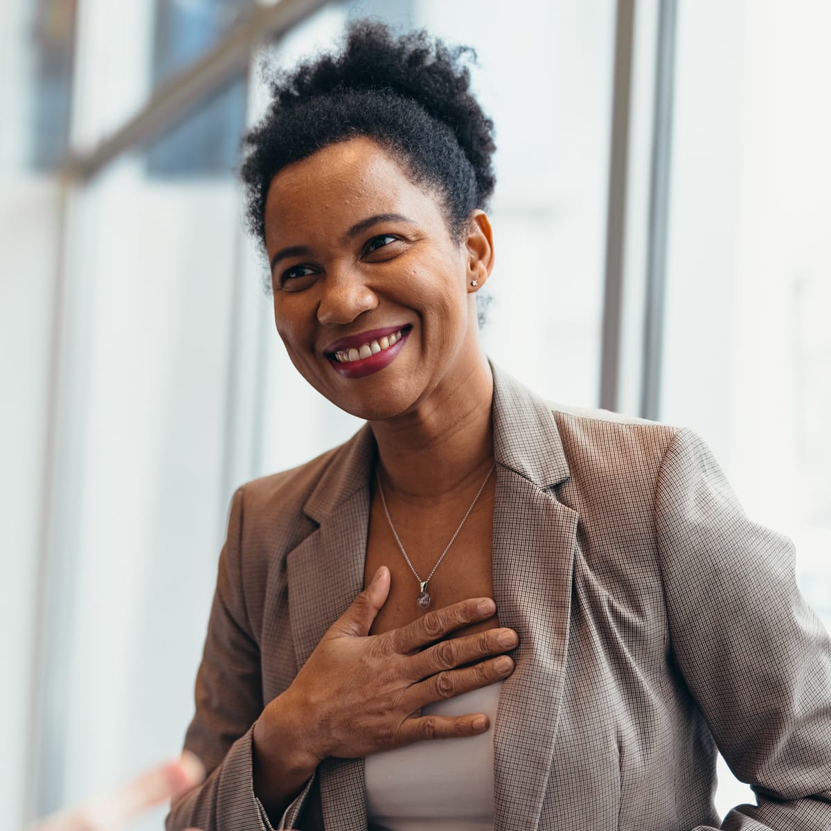 Smiling woman in a blazer with one hand over her heart