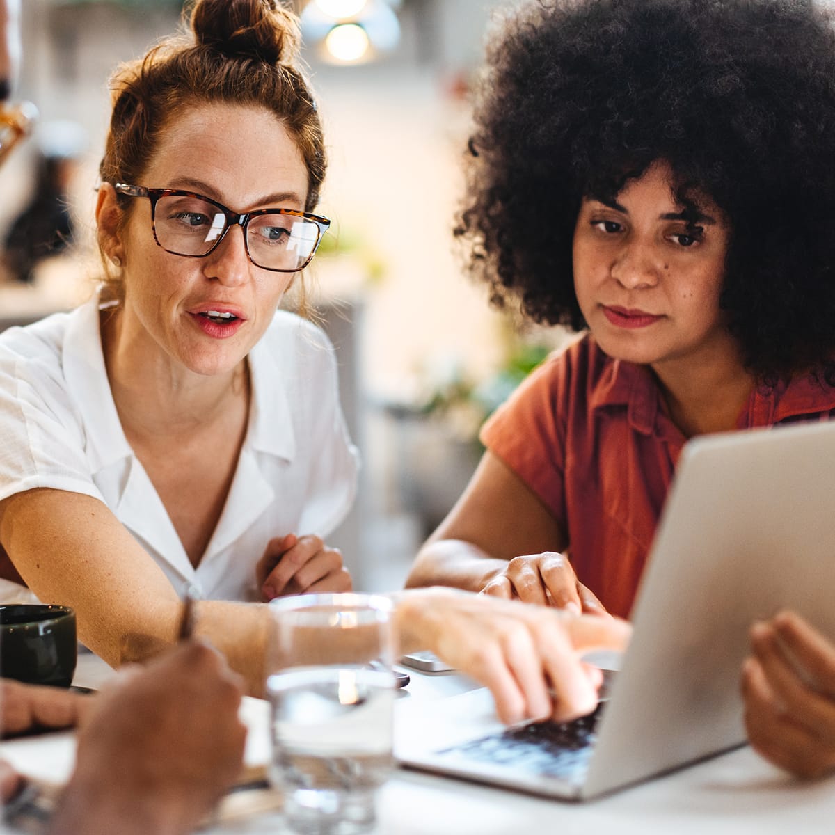 Two women collaborate around a laptop at a table in a café