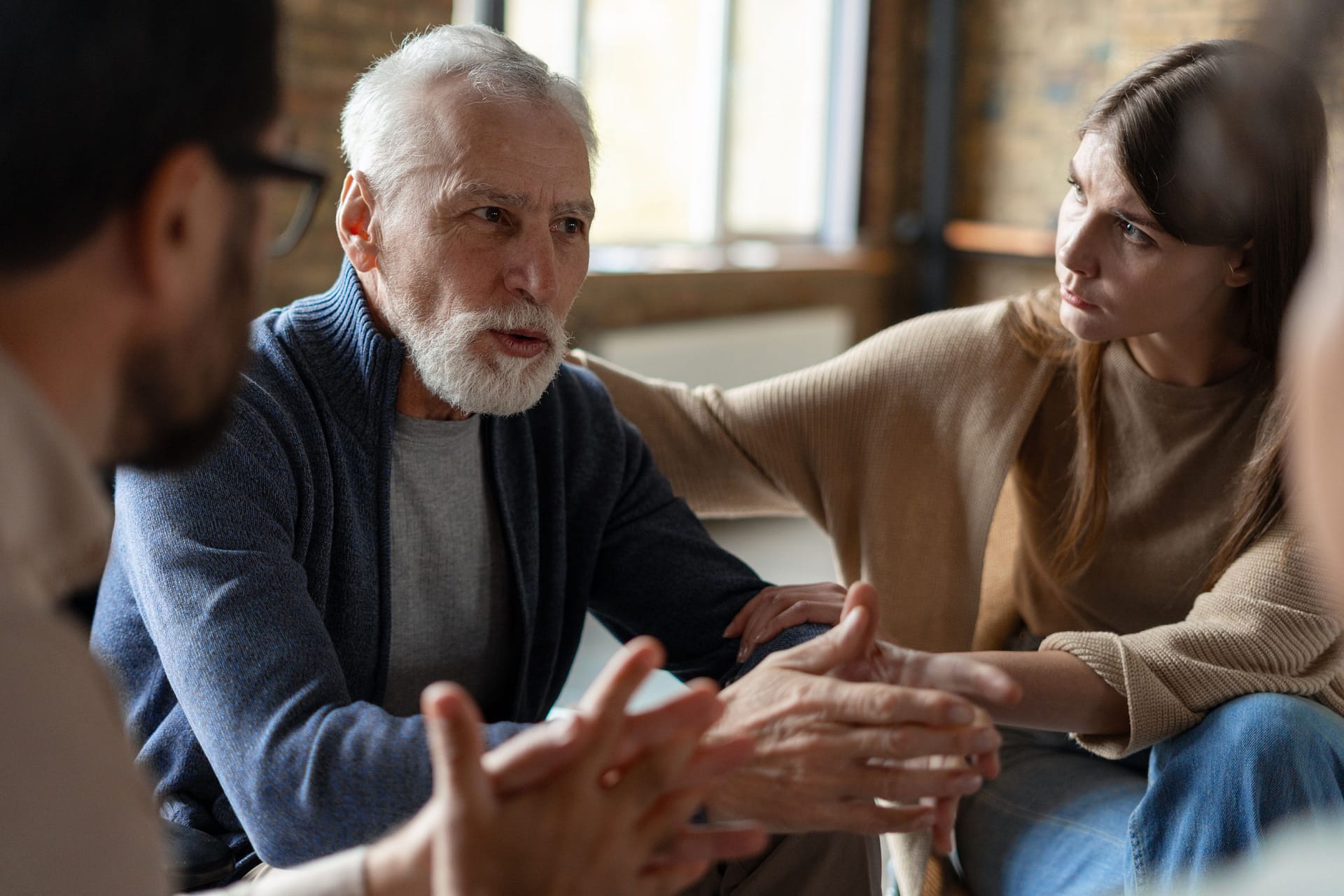 An older man and woman participate in a discussion with others in a warmly lit room